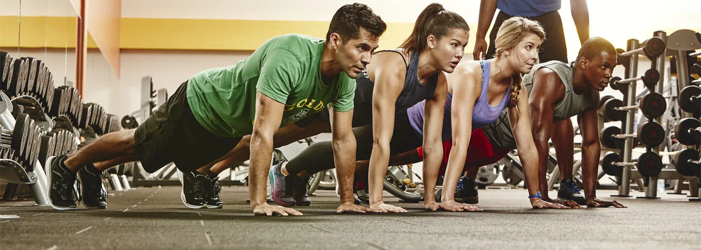 A group of people in athletic clothing are engaged in a plank exercise in a fitness center setting.