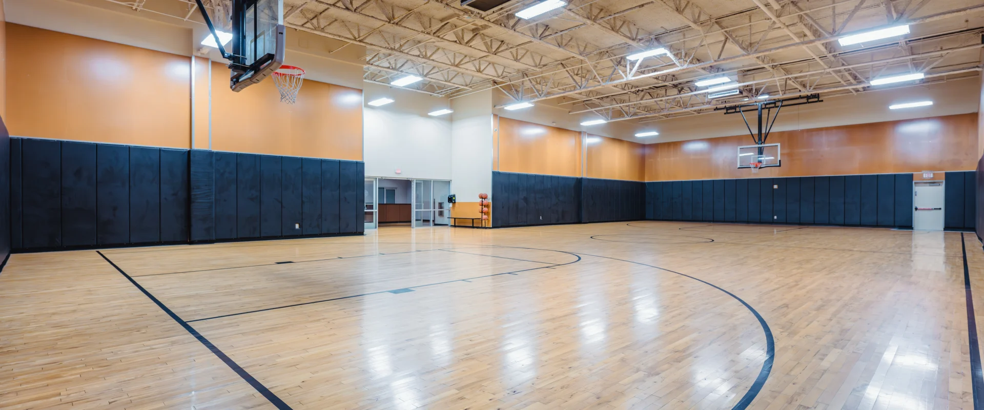 Full-sized indoor basketball court with polished wood flooring, black padded walls, and two basketball hoops at Gold's Gym San Marcos.