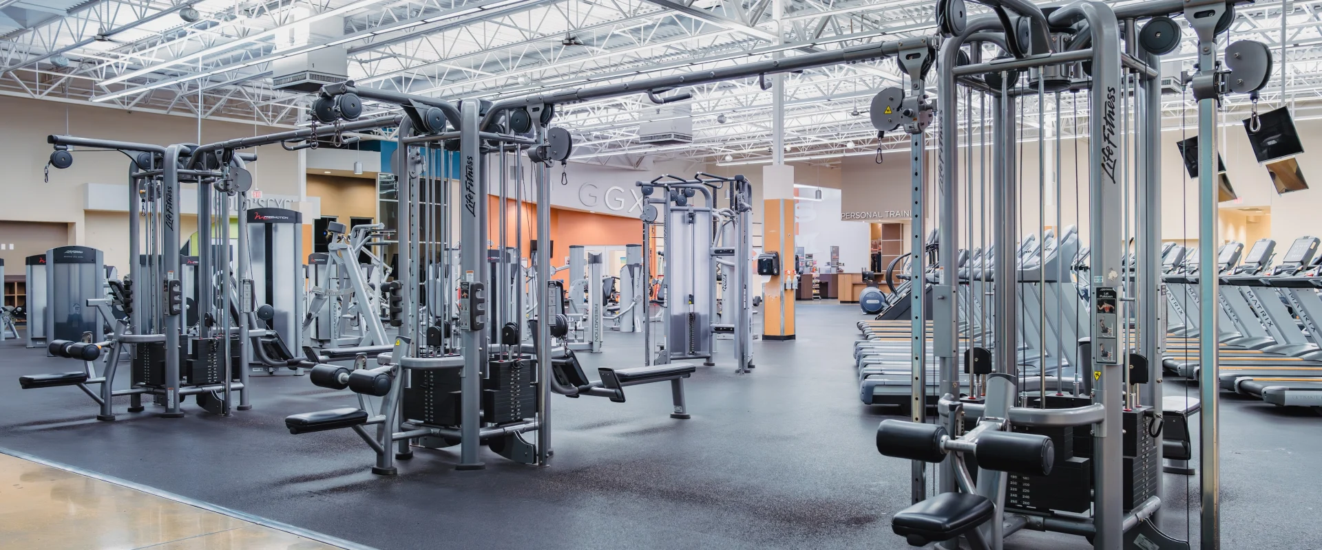 Spacious gym interior with various exercise machines, including weightlifting and cardio equipment. Bright lighting and a clean, organized layout.