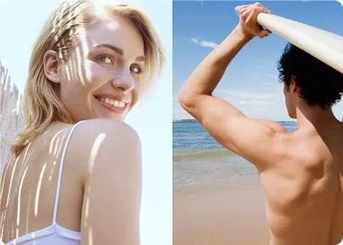 A smiling woman with blonde hair stands in the foreground, while a shirtless man is visible in the background on a beach with a clear blue sky.