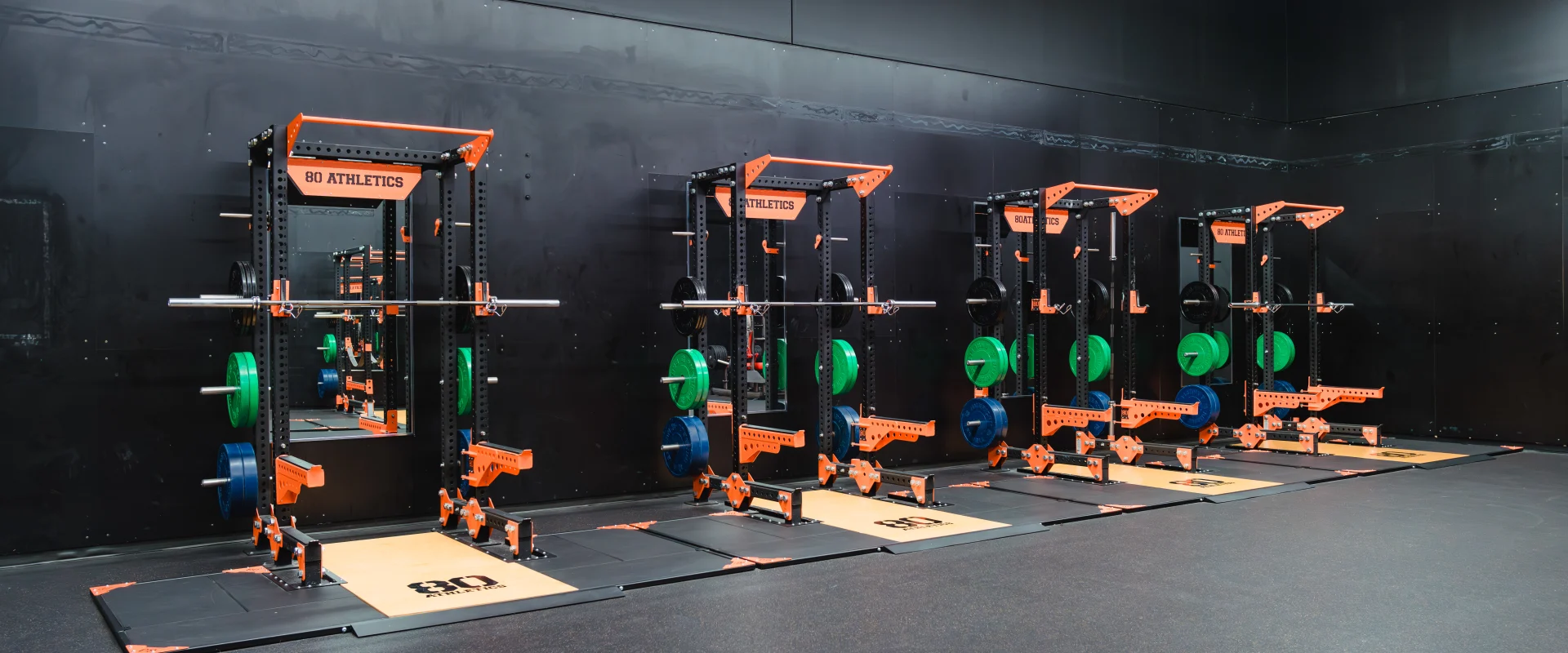 An Olympic lifting area at Gold's Gym featuring vibrant orange and black lifting racks, platforms, and weight plates set against a sleek black wall.