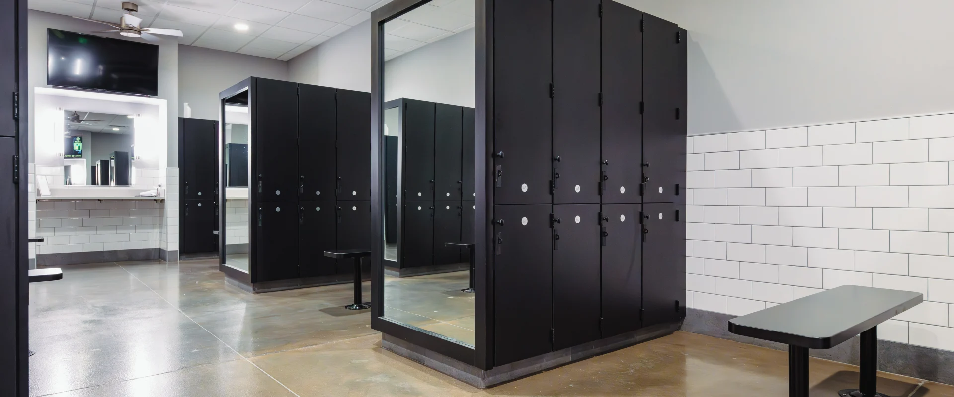 Locker room at Gold’s Gym Belterra, featuring sleek black lockers, a large full-length mirror, tiled walls, polished concrete floors, and modern vanity stations with bright lighting.