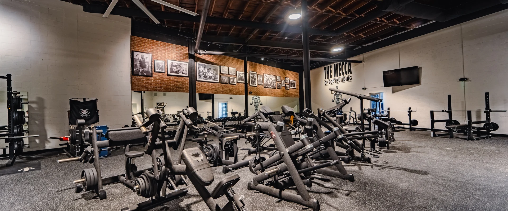 Strength training area at Gold’s Gym (Gas Worx) with rows of plate-loaded machines and “The Mecca of Bodybuilding” wall.
