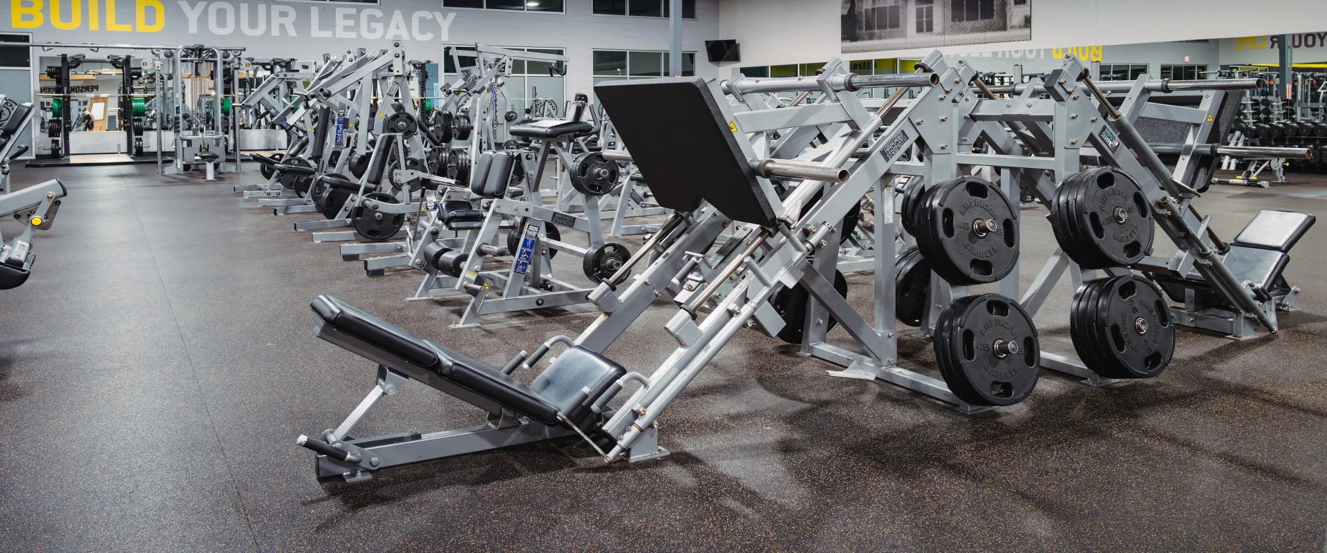 The plate-loaded area at Gold’s Gym in Slaughter & South Congress features a variety of strength training equipment designed for targeted muscle workouts. The machines are equipped with black weight plates and adjustable seating to accommodate different exercises. The layout provides ample space between equipment, with rubberized flooring for safety and durability. Mirrors line the walls, enhancing visibility and form-checking during workouts, while motivational wall graphics add energy to the space.