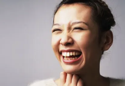 A woman with a wide, joyful smile, her face filling the frame against a plain gray background.
