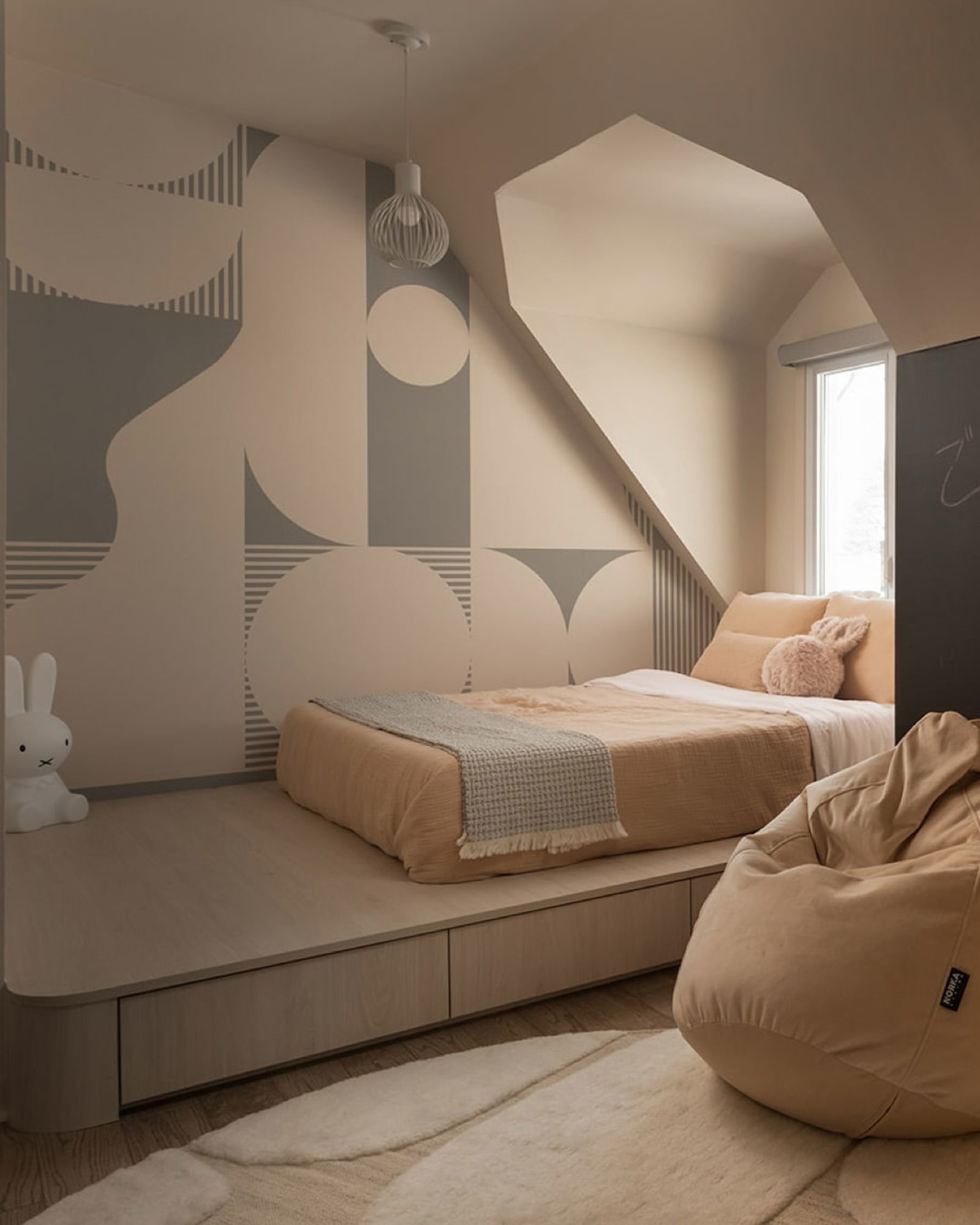 A cozy bedroom nook featuring a geometric accent wall, a white dresser, and a collection of plush toys.