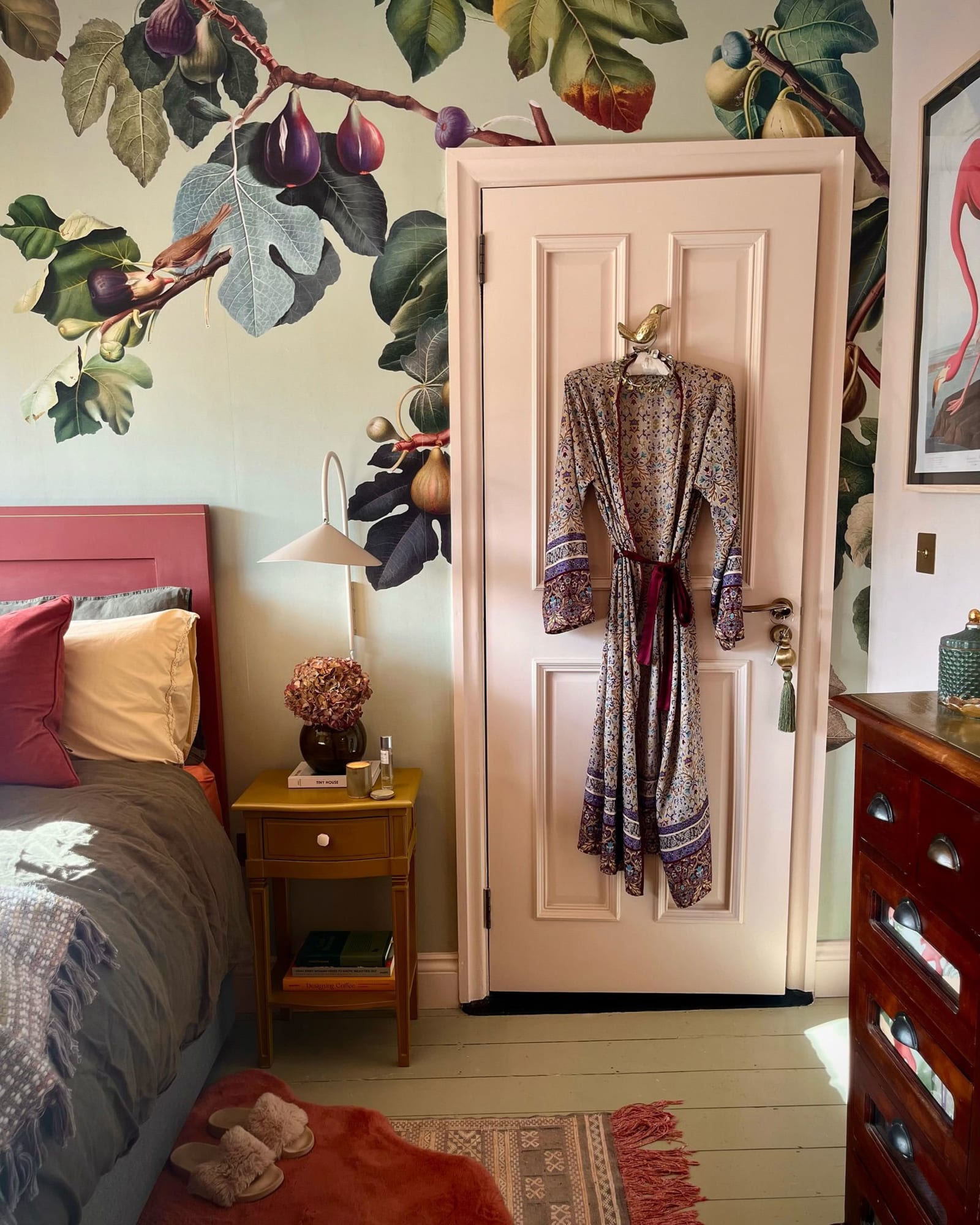 A warm, inviting bedroom with a pink botanical wallpaper behind a gingham bed and mint green nightstand.