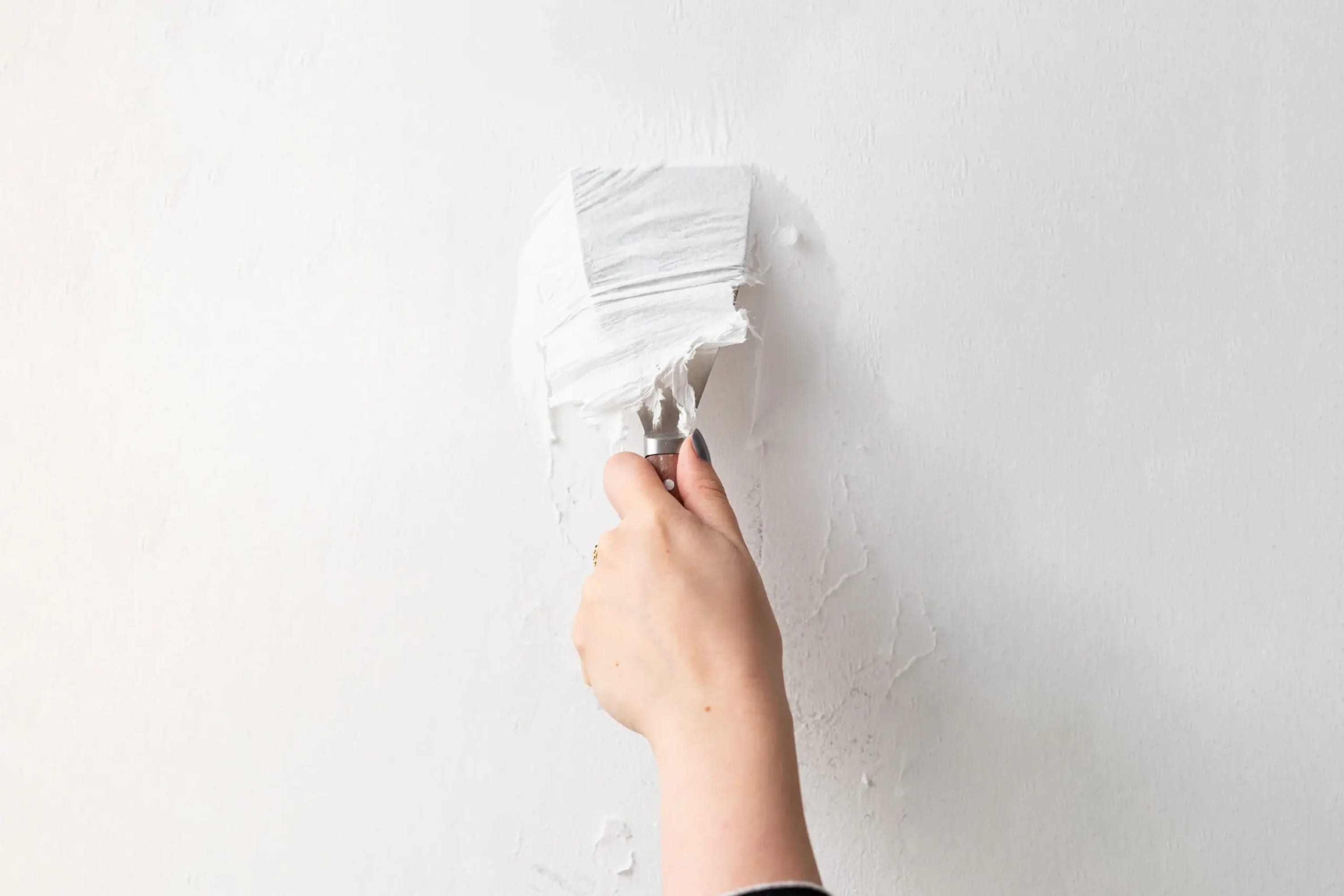 A person applies white filler to a wall with a putty knife.