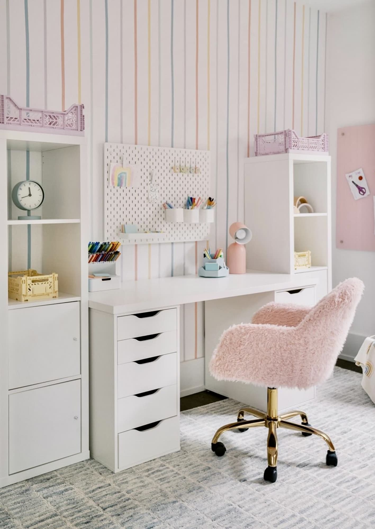 A stylish teen study space with vertical pastel-striped wallpaper, a white desk, and a pink faux fur chair.