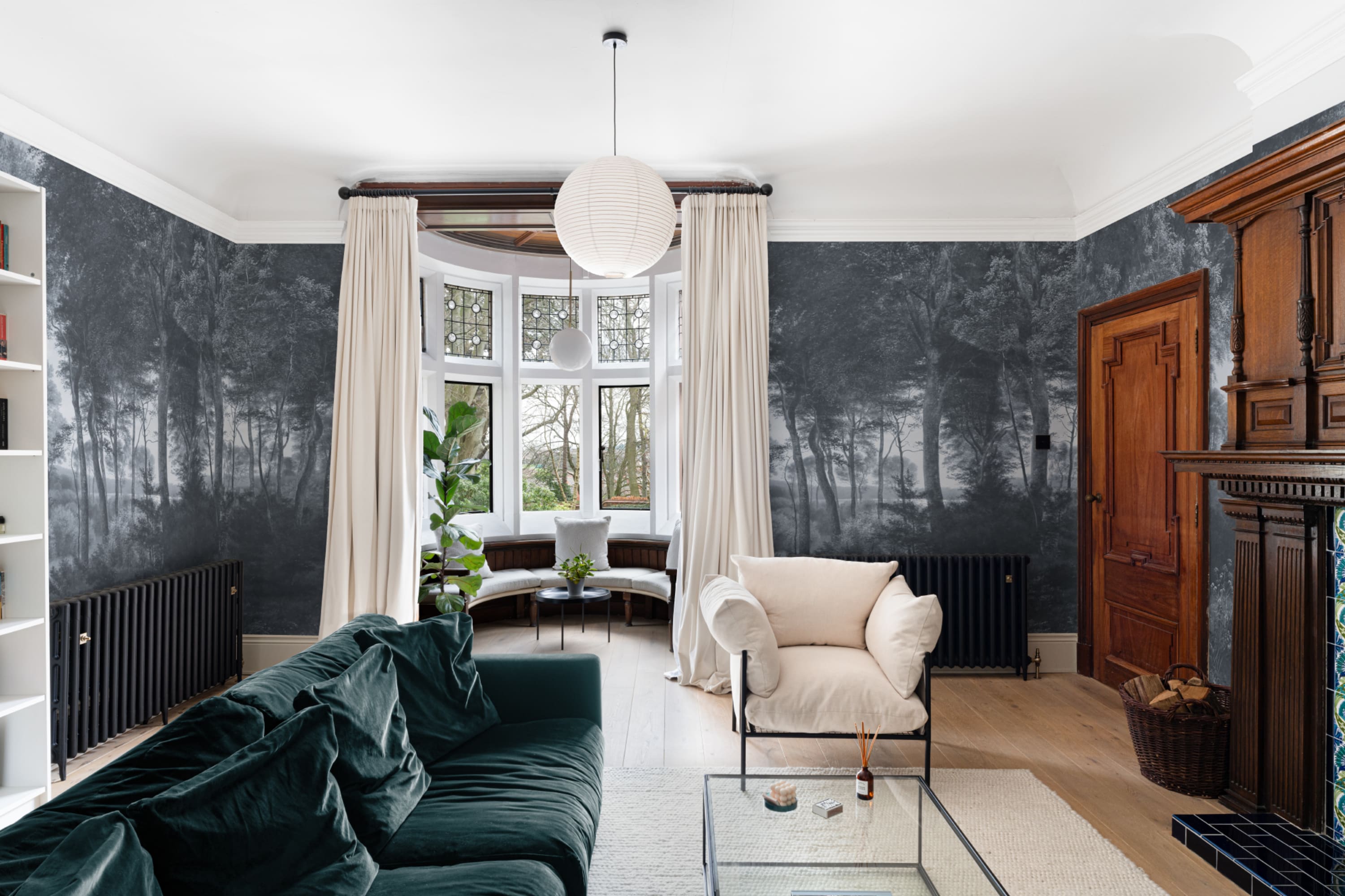 Living room with dark green velvet sofa and white armchair set against a dramatic grayscale forest mural.