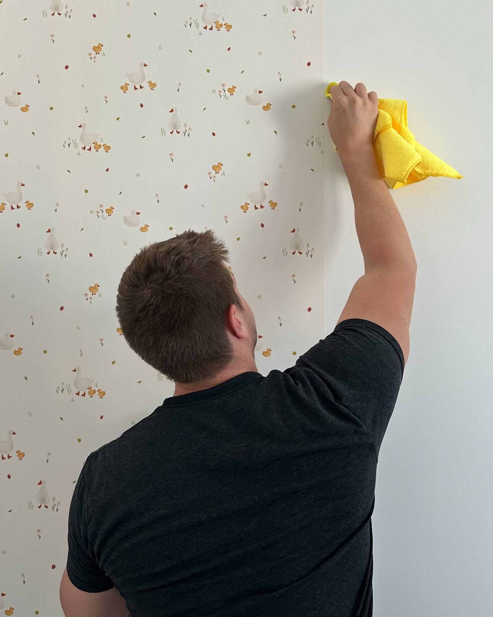 A man installing peel-and-stick wallpaper to a nursery wall.
