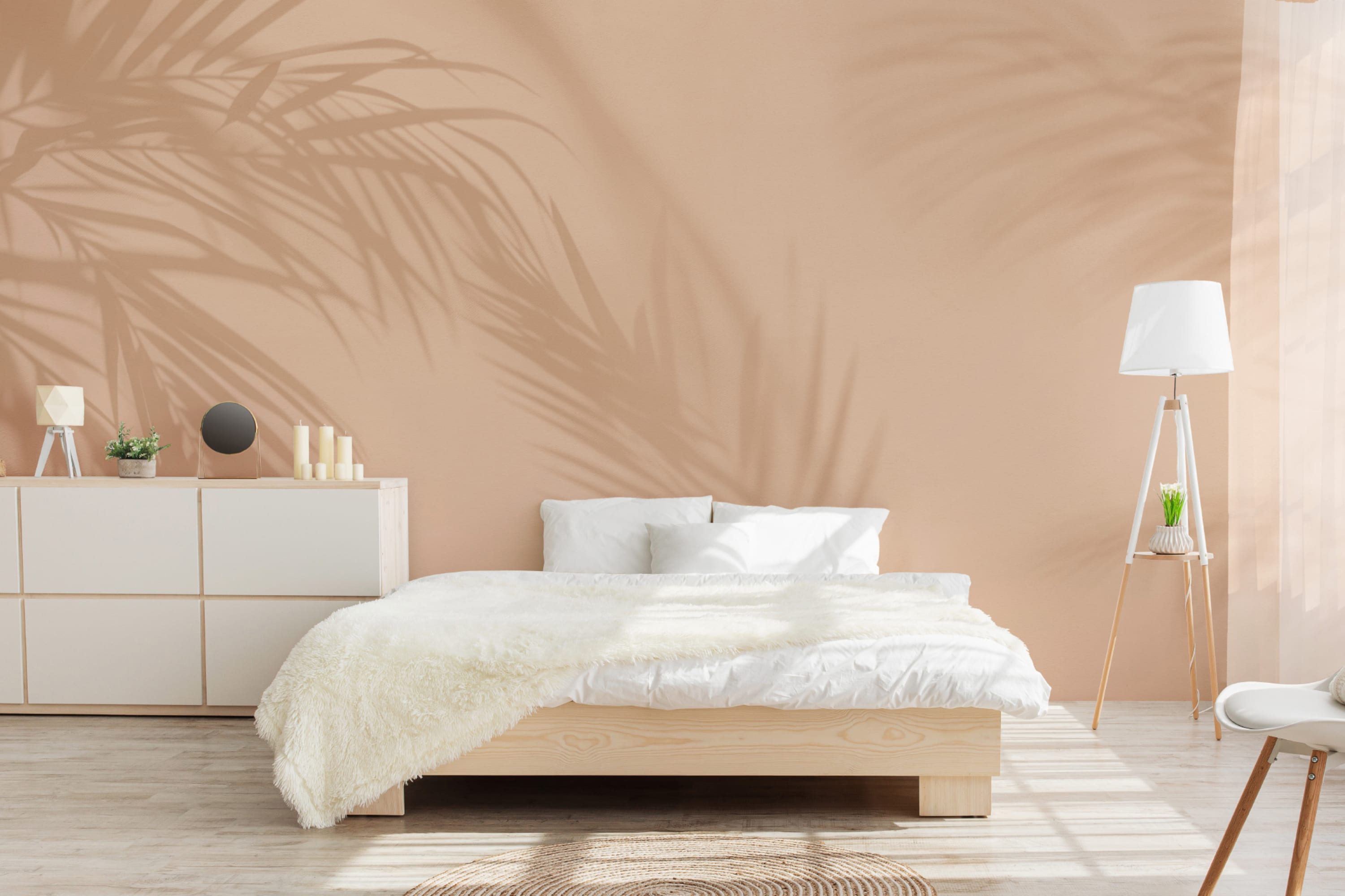 Bright bedroom with peach wall showing palm shadows and minimalist decor.