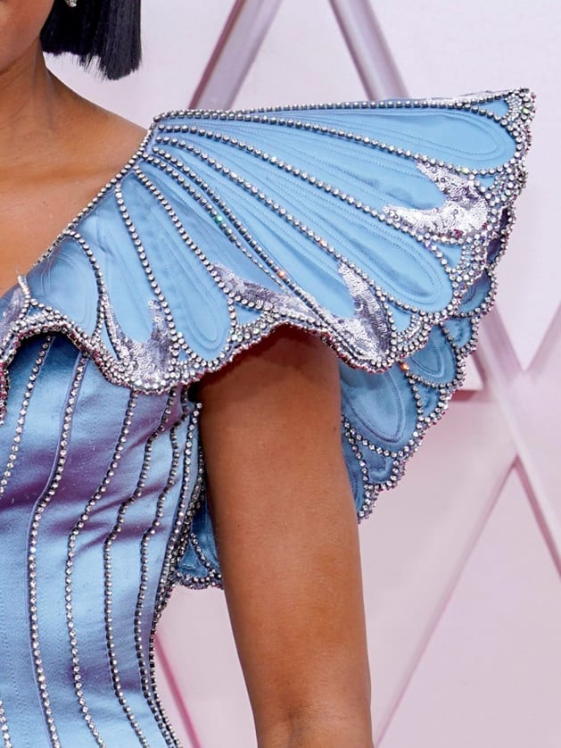 Foto mostrando os detalhes da manga bufante do vestido de Regina King, com os cristais e lantejoulas prateadas aparecendo.