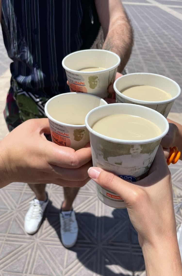 Foto para ilustrar uma das dicas 4 bebidas e pratos típicos de Valência. Quatro copos de papel com uma bebida bege, orchata de chufa, estão brindando.