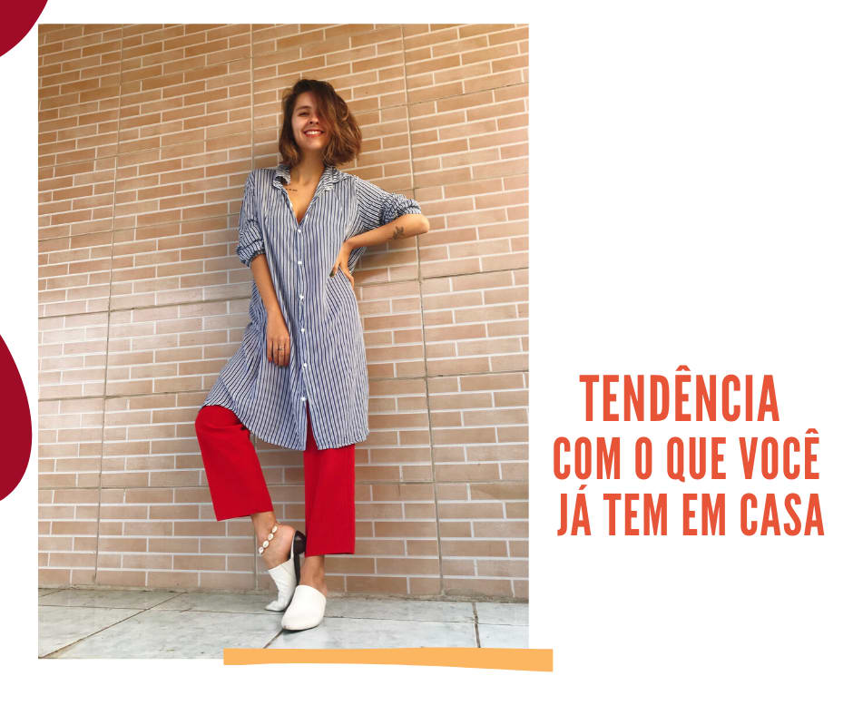 Montagem com fundo branco, uma imagem alinhada à esquerda com a seguinte frase em laranja, escrita com letras maiúsculas: "TENDÊNCIA COM O QUE VOCÊ JÁ TEM EM CASA". Na foto, Marcie posa em frente a uma parede com tijolinhos laranjas e chão branco. O look é composto por camisa oversized na altura do joelho listrada em azul e branco, calça de alfaiataria vermelha, mule branco com salto geométrico.