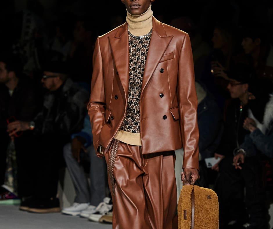 Foto de abertura do post sobre moda masculina de 2023 de outono. O look é composto por terno de couro marrom, blusa de gola alta bege de gola alta.