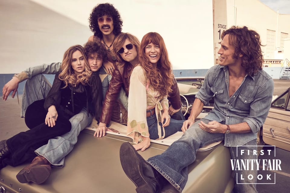 Foto do elenco de Daisy Jones & The Six em cima de um carro. São 4 atores e 2 atrizes sorrindo, com roupas setentistas, pantalonas, camisas amplas e muito jeans.