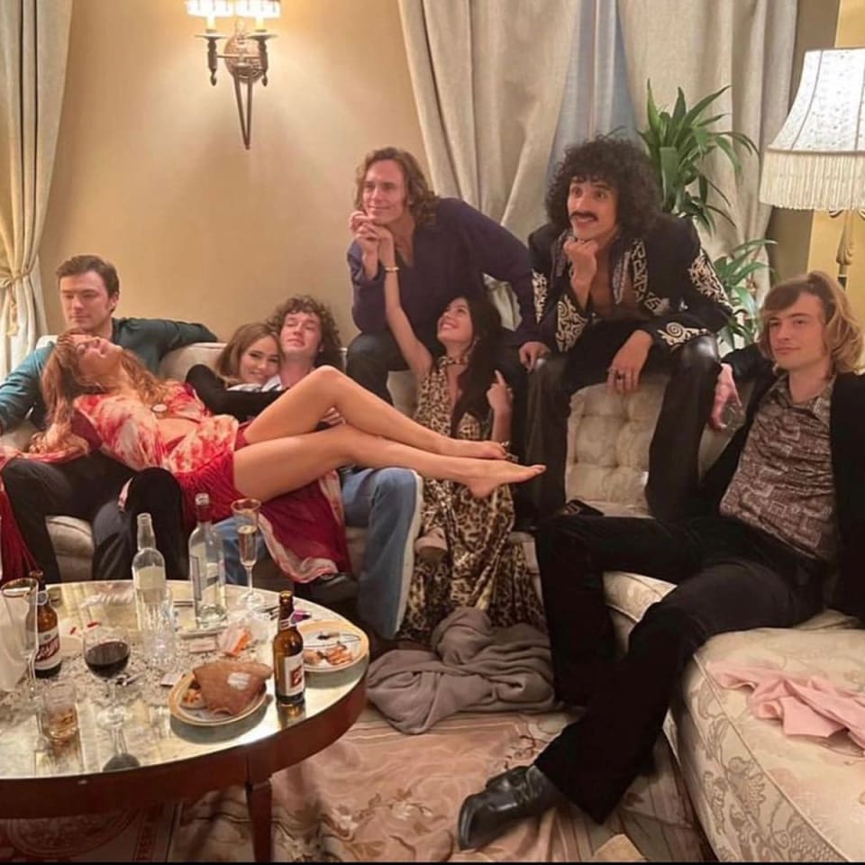 Foto de Daisy Jones & The Six para ilustrar as mudanças entre o livro e a série. Na foto, o elenco da série está caracterizado como seus personagens, mas todos sentados juntos em um sofá de hotel.