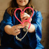 Photo of a woman holding a pink stethoscope shaped into a heart by Patty Brito on Unsplash