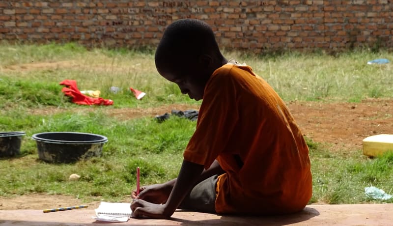 A photo of a young boy sitting and writing in a book by Stijn Kleerebezem on Unsplash