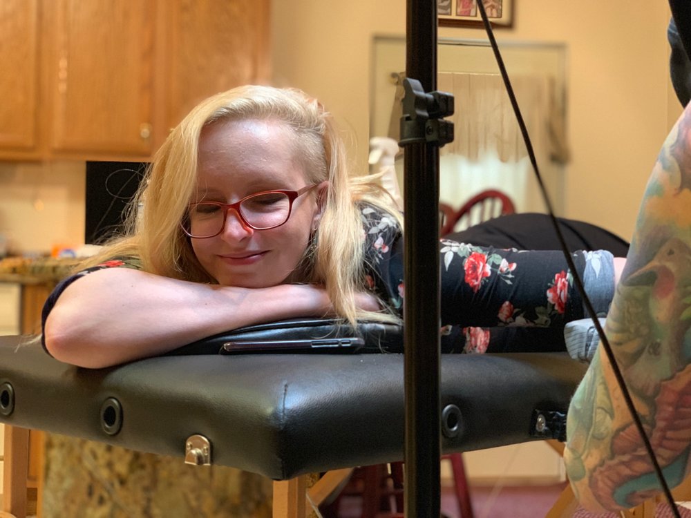 Sally smiling as she lies on a table while getting a tattoo on her arm