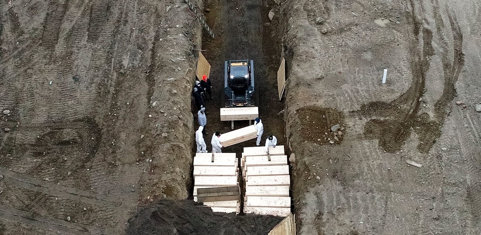 עובדים לבושים בבגדי מגן קוברים קורבנות של וירוס הקורונה בתעלה ליד ניו יורק / צילום: Associated Press, John Minchillo