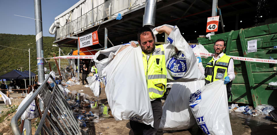 עובד זק"א סוחב שקיות מלאות כובעים לאחר האירוע בהר מירון / צילום: Reuters, מירון