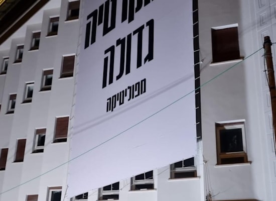 מיכה קאופמן, מנכ''ל פייבר, עומד מתחת לבניין עם שולחן של בקבוקי מים לכל דורש. על הבניין, לוגו החברה בצבעי הגאווה מיכה קאופמן, מנכ''ל פייבר, עומד מתחת לבניין עם שולחן של בקבוקי מים לכל דורש. על הבניין, לוגו החברה בצבעי הגאווה