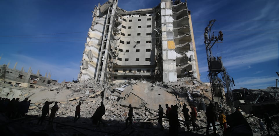 פלסטינים עוברים ליד בניין שנהרס בתקיפה ישראלית ברפיח / צילום: Associated Press, Hatem Ali