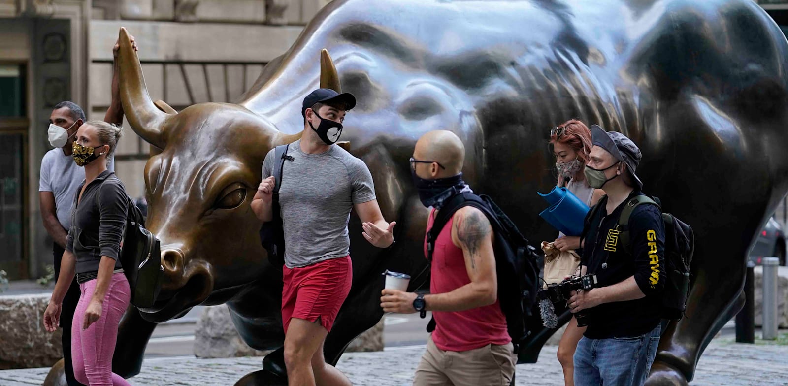 צעירים חולפים על פני פסל השור בוול סטריט, ניו יורק / צילום: Associated Press, Mark Lennihan