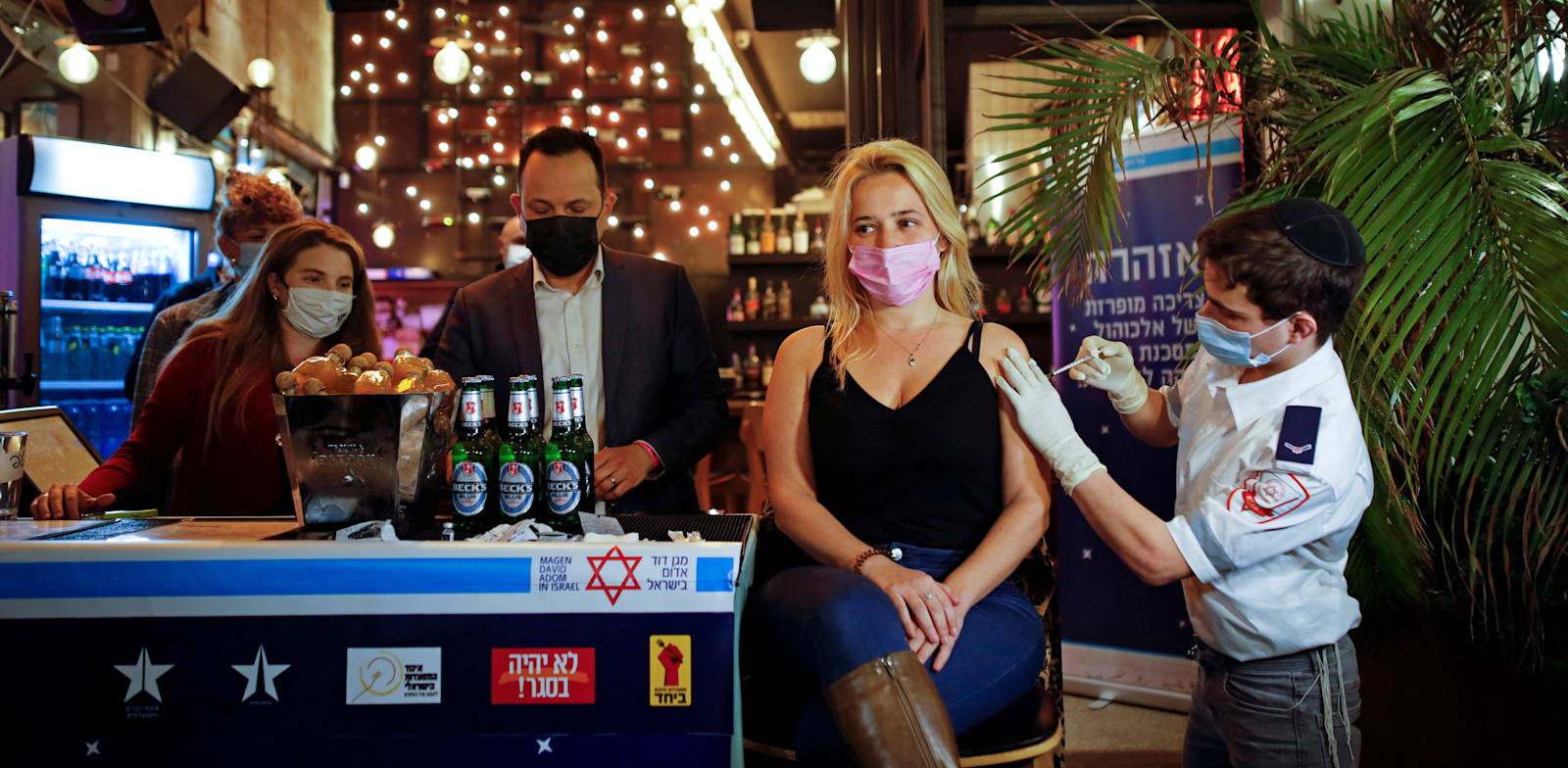 אישה מקבלת חיסון לקורונה בפאב, כחלק מיוזמה של עיריית ת"א שמציעה משקה לכל מתחסן / צילום: Reuters, Corinna Kern