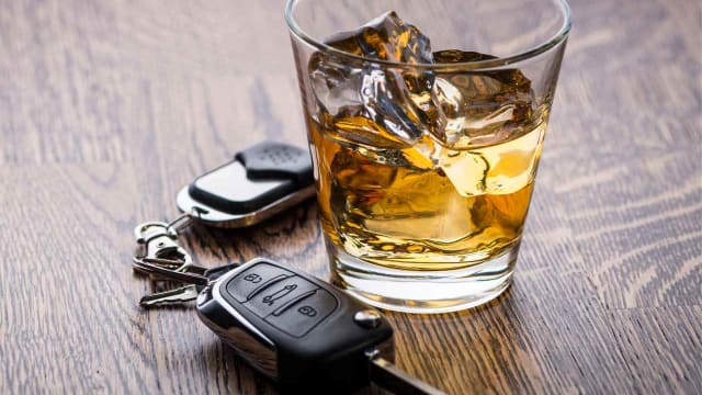 a glass of alcohol and car keys on a wooden table