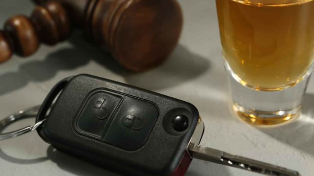 a glass of whiskey, car key, and gavel on a white desk