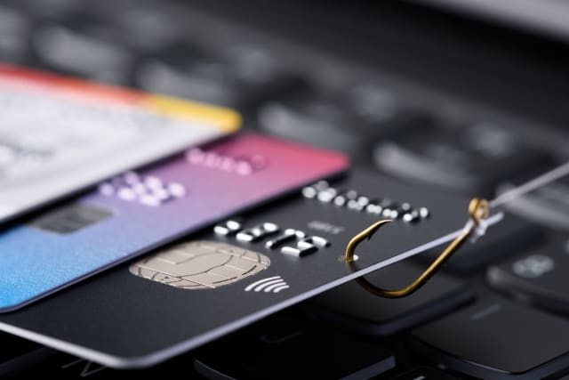 Credit cards on a laptop keyboard with a fishing hook hooked into one.
