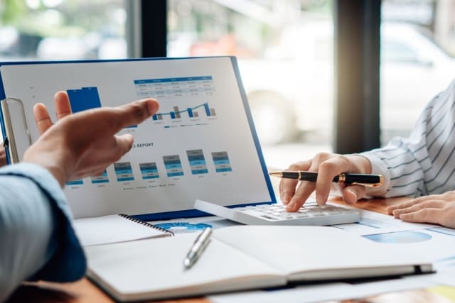 close-up of two people reviewing financial charts on a clipboard.