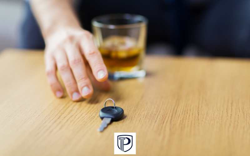 a man reaching for car keys next to a glass of whiskey