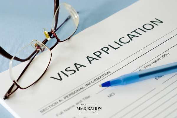 a pen, visa application, and glasses on a blue table