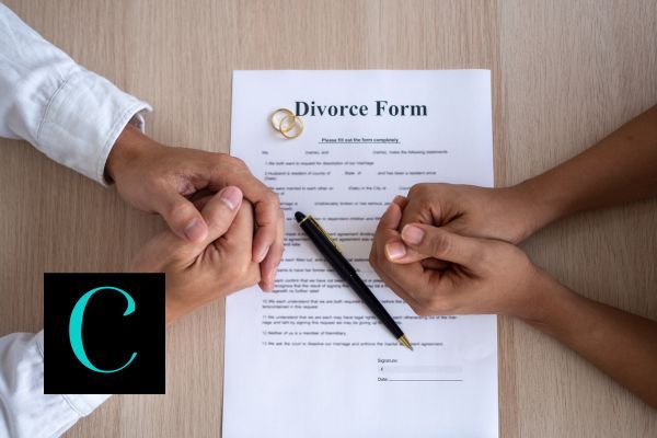 a couple sitting at a table with divorce papers and their wedding rings in between them