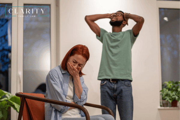 A sad woman with her hand over her mouth with a man behind her with his hands on his head in frustration