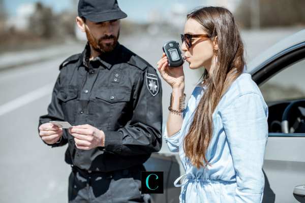 a woman next to a car taking a breathalyzer test