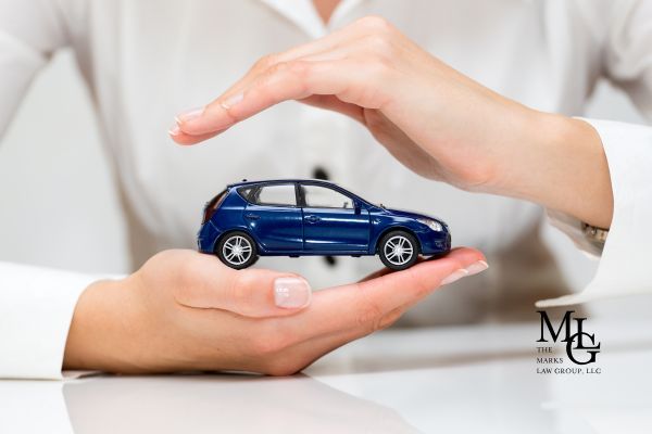 Hands cupping a small blue model car, symbolizing car insurance protection.