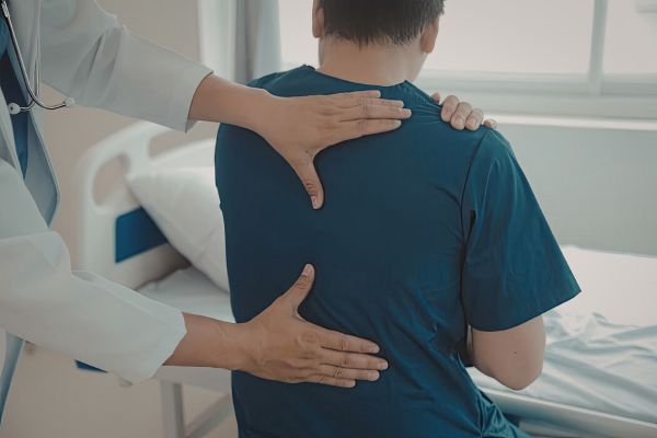 A doctor examines a patient’s back and shoulder in a clinical setting.