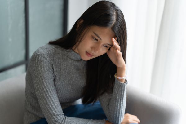 Woman sitting on a couch, holding her head and looking stressed or worried.