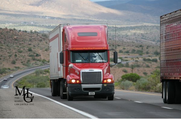A red semi-truck driving on a winding highway through a desert landscape.