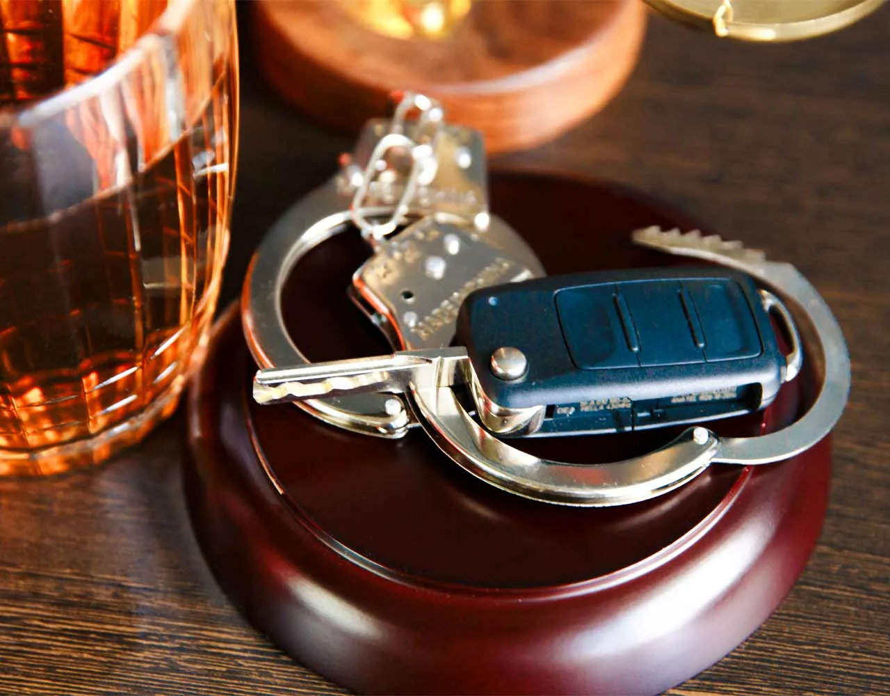 Handcuffs and a car key next to a glass of alcohol.