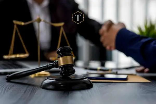 Gavel and scales of justice on a desk with a handshake in the background.