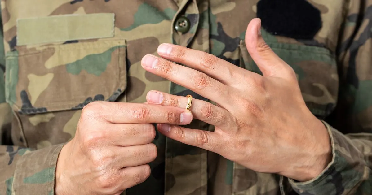 A person in military uniform removing a gold wedding ring from their finger, symbolizing a military divorce or separation.