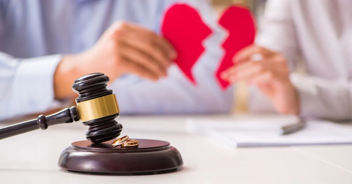 Gavel and two wedding rings on a desk in front of a couple tearing a heart in half.