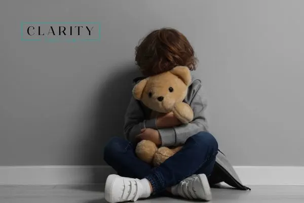 Young child sitting in front of gray wall hugging a teddy bear