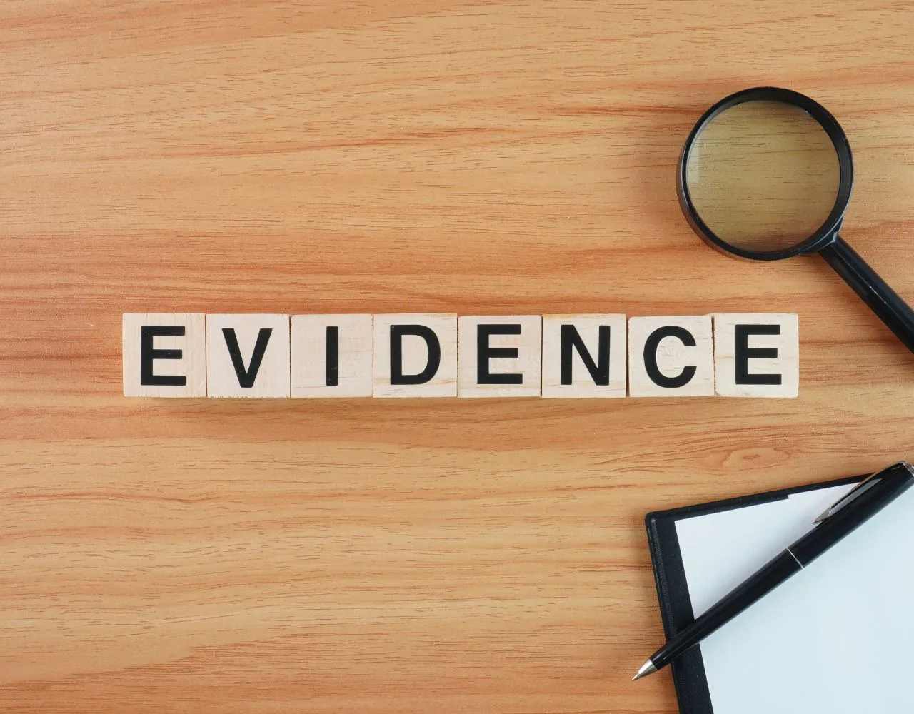 Wooden tiles spelling "EVIDENCE" with a magnifying glass and a clipboard on a wood grain surface.